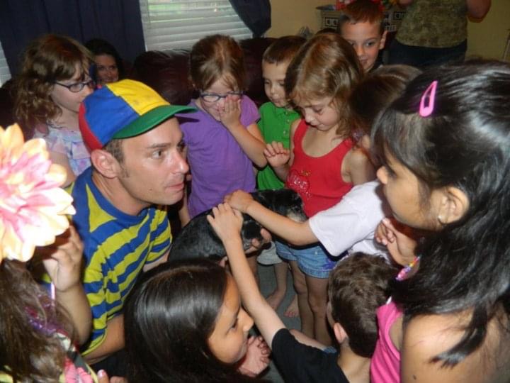 Children enjoying party with entertainer in colorful attire.