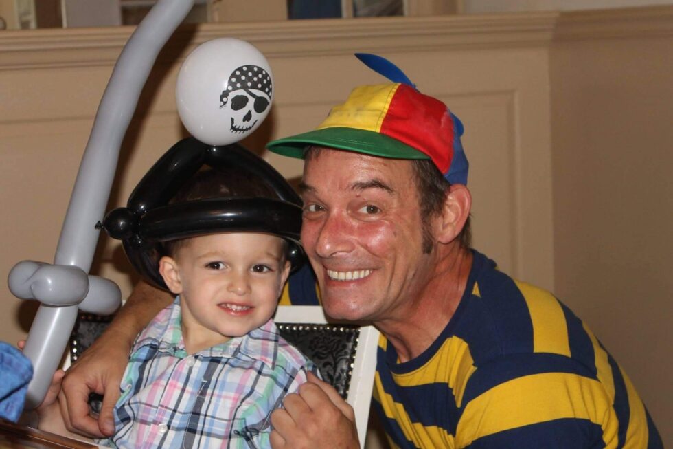 Man and child smiling, child wearing balloon pirate hat.