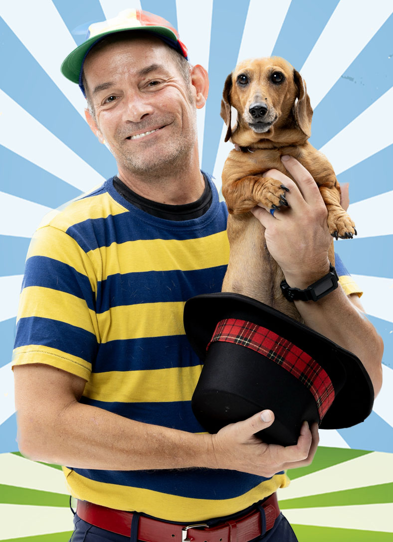 Man holding dachshund and smiling with hat.
