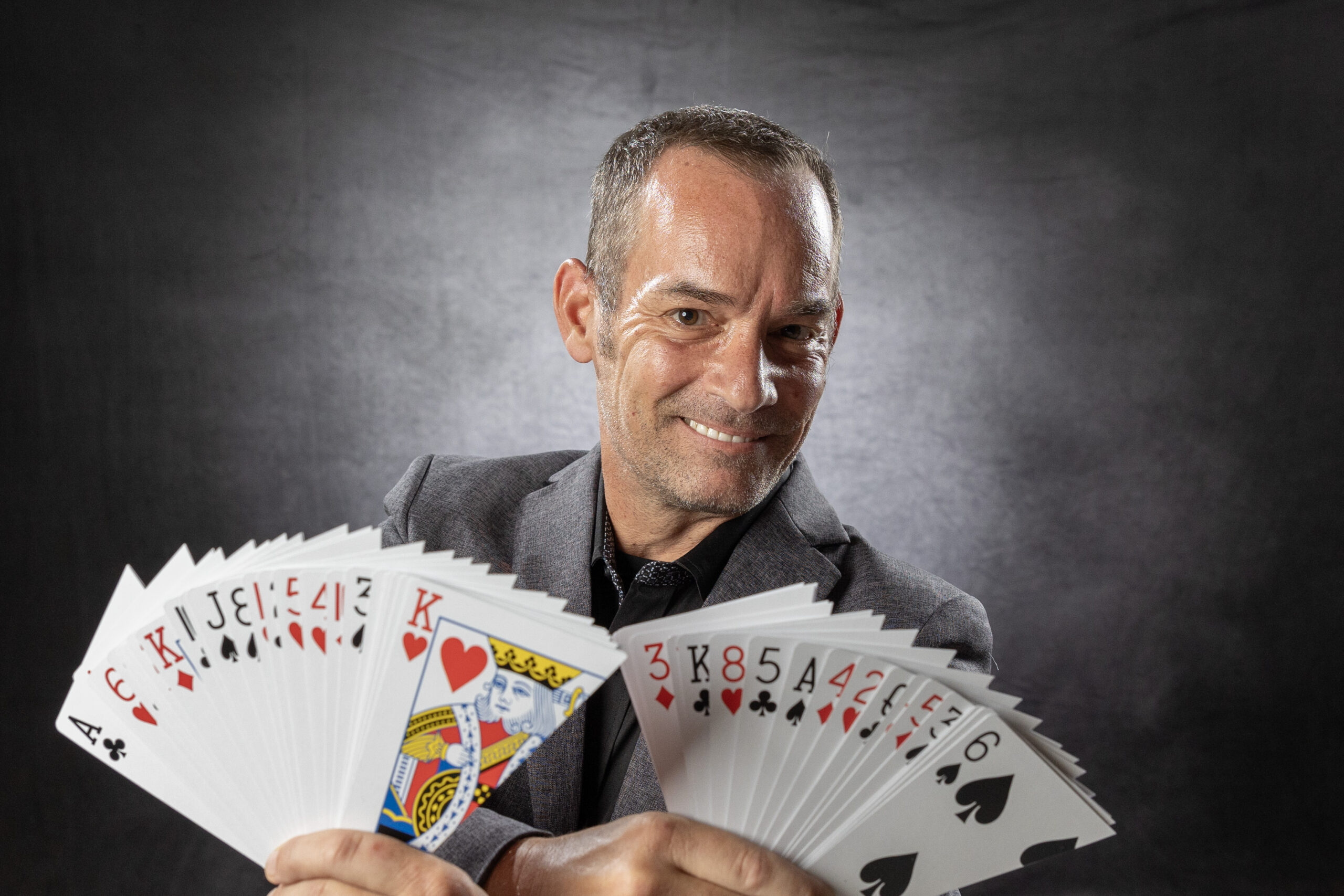 Man smiling while presenting a fan of playing cards.